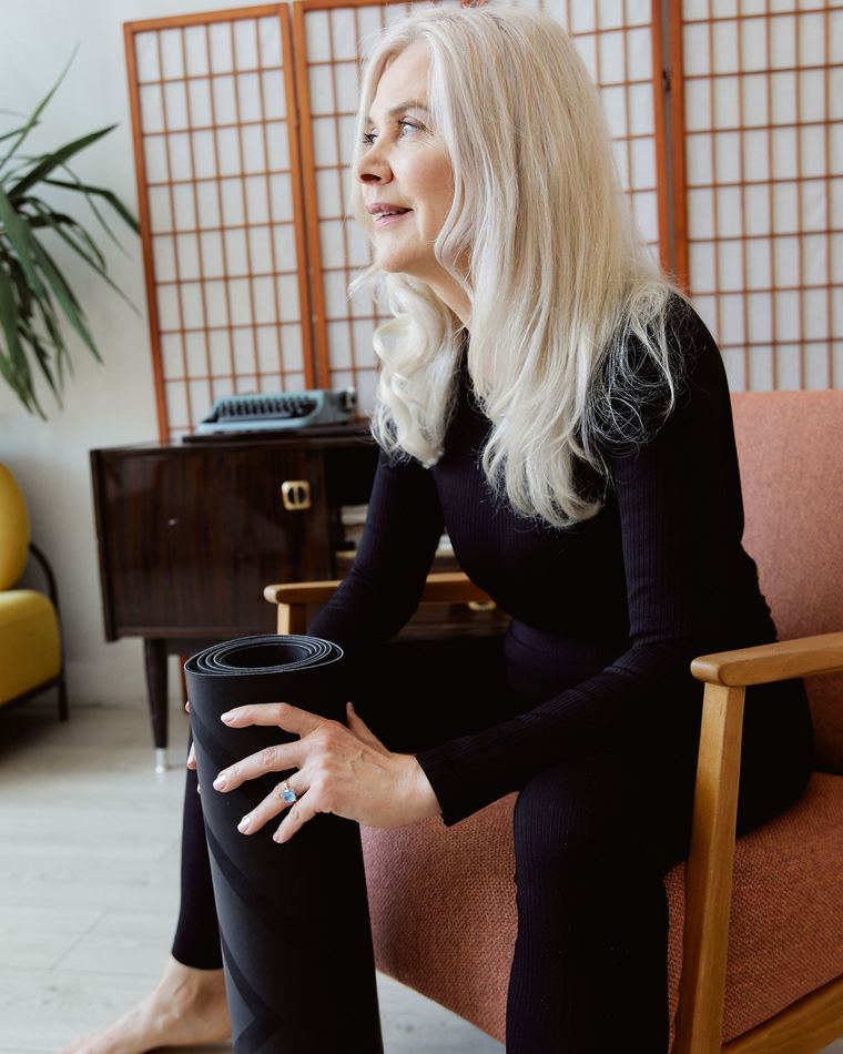 Une femme aux cheveux blancs, assise dans un fauteuil, son tapis roulé posé à côté d'elle.