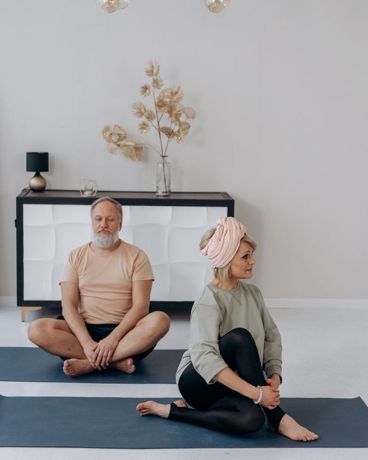 Un homme assis en tailleur, les yeux fermés, et une femme en torsion douce assise sur son tapis.